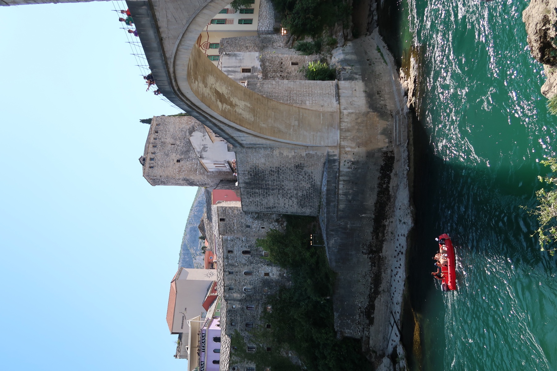 The stone arch of the Old Bridge in Mostar above the green river, with a red boat below